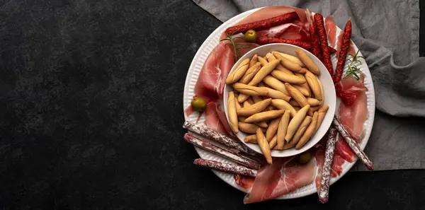 İspanyol jamonu, Chorizo çubukları ve picos ekmek çubukları olan düz bir tabakta, karanlık masada, kopyalama alanı. Tapas kavramı