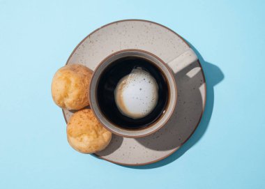 Brezilya peynirli ekmekli bir fincan kahvenin üst görüntüsü. Mavi arka planda Pao de queijo.