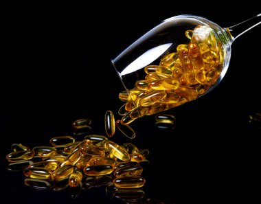 Balık yağı kapsülleri. Koyu siyah kavanozda sarı omega 3 hapları. Şarap kadehinde balık yağı kapsülleri. Kavanozda Kova ampulleriyle. Siyah üzerine izole edilmiş.