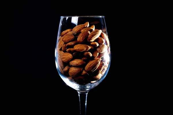 Peeled almond in jar glass bucket on a black isolated background. Row of bowls with almond nuts, front view. Peeled almond pattern