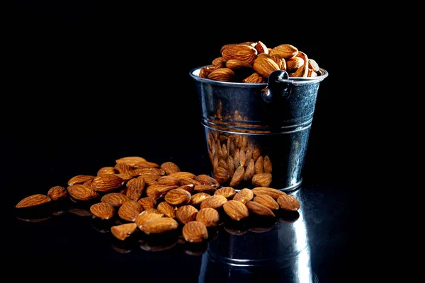 Peeled almond in jar glass bucket on a black isolated background. Row of bowls with almond nuts, front view. Peeled almond pattern