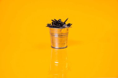 Bir sürü metal vida, bir bardakta, kova kavanozunda çelikten yapılmıştır. Metal için kendi kendine dokunan vida, demir, krom kaplama kendi kendine dokunabilen vida, turuncu sarı bir arka planda, metin için boşluk