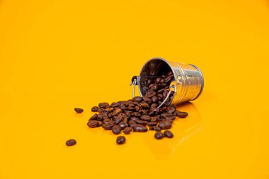 Kavrulmuş kahve çekirdeklerini bir bardakta, kova kavanozunda düşürdüm. Metal için kendi kendine dokunan vida, demir, krom kaplama kendi kendine dokunabilen vida, turuncu sarı arka planda izole edilmiş.