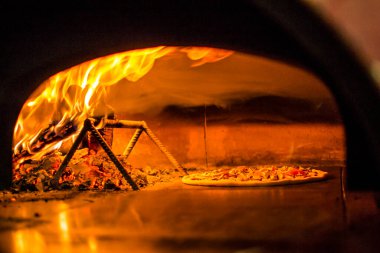 Fırında pizza pişirmek. Taş ocağın yanındaki pizzada ateş var. Şöminesi olan geleneksel bir pizzacının arka planı..