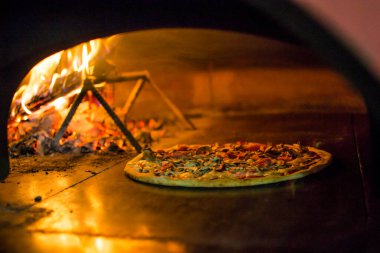 Fırında pizza pişirmek. Taş ocağın yanındaki pizzada ateş var. Şöminesi olan geleneksel bir pizzacının arka planı..