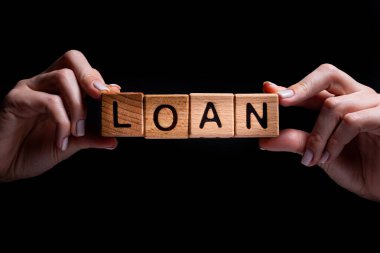 Kadın eli, içinde harfler olan bir küp, kira satışı, alım-satım ve kredi olan tahta küpleri tutuyor. Siyah arka planda tasarımcı için proje. Kelimeler evde öğrenilir, sağlık...