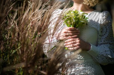 Beyaz gelinlikli gelin elinde bir buket beyaz çiçek tutuyor. Şakayıklar, güller. Düğün için. Gelin ve damat. Hoş geldin buketi. Düğünlerin farklı yapraklarla süslenmesi