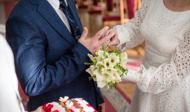 Yüzüklü gelin ve damadın elleri. Gelin ve damat bir kafede. Ahşap bir masada düğün buketi. Gelin ve damat birbirlerinin elini tutuyorlar. Evlilik yüzükleri. Bir kafede birbirini seven bir çift. Aşıklar için sıcak çay