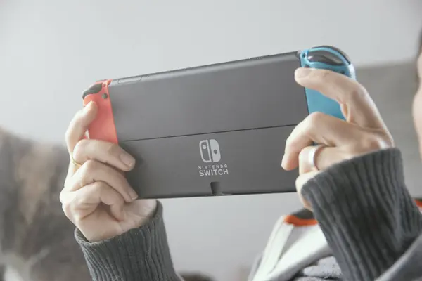 Barselona, 1 Aralık 2023: Nintendo Switch marka taşınabilir konsolla oynayan genç kadın evdeki kanepede oturuyor..
