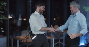 Başarılı şirket patronları zaferi kutlayan ve yönetime çözüm getiren el sıkışıyorlar. Karanlık ofis içi. Heyecan.
