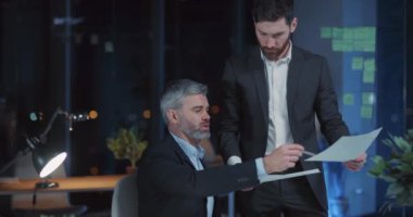 Kafkasyalı işletme yöneticileri uzun saatler boyunca çalışıp karanlık ofis içinde mali planlarını tartışıyor..