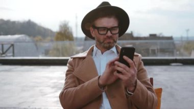 Gözlük takan şık bir adam ve şık bir şapka dışarıda, doğada akıllı telefonuyla meşgul.