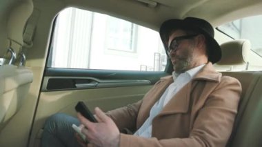 Çekici, olgun bir adamın araba sürerken akıllı telefonuna göz attığı profil. Güzel şehirde taksiden inen İngiliz iş adamının yakın çekimi..