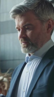 Ciddi gri saçlı başarılı iş adamının portresi resmi giysiler içinde akıllı telefonu elinde tutarak sohbet ediyor. Şirket yöneticisinin bulanık arka planda cihaz kullanırken çekilmiş yakın çekim görüntüleri. Kapalı