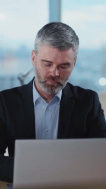 Odaklanmış profesyonel bir adam, şık ve şık bir ofis ortamında özenle bir dizüstü bilgisayar üzerinde çalışıyor.