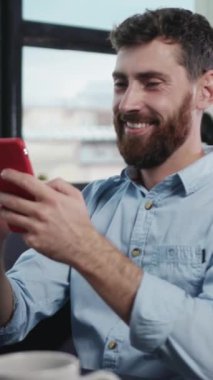 Şık, modern bir çalışma alanında akıllı telefonuyla derinden ilgilenen odaklanmış bir adam konsantrasyon ve yaratıcılık yayıyor.