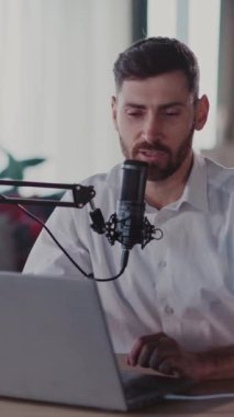 Bu videoda, masada dizüstü bilgisayarı ve mikrofonu olan sakallı bir adam görülüyor. Şarap şişesiyle gülümsüyor, cazibe yaratıyor.