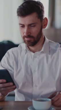Sıcak bir kafede, bir adam telefonunu kontrol eder ve kahvesini yudumlar. Daha sonra bir tablete geçiyor, bağlı kalarak içkisinin tadını çıkarıyor.