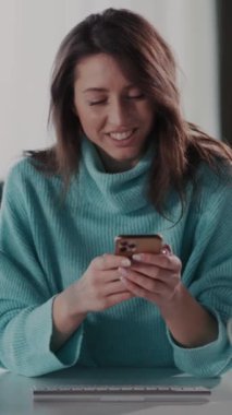 Mavi kazaklı bir kadın masada oturuyor ve cep telefonuyla konuşuyor. Mikrofona göre bir röportajda olabilir, odaklanmış ve meşgul.