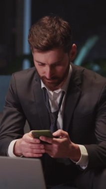 Neşeli, çekici, genç, yetişkin bir iş adamı. İnternette akıllı telefondan mesaj yazıyor. Dizüstü bilgisayarla apartman dairesinde oturuyor..