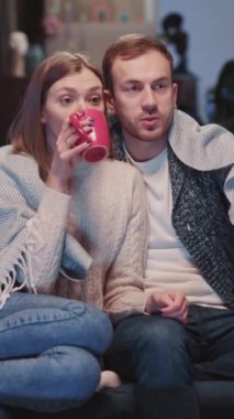 Genç çift, oturma odasındaki koltukta Noel ağacıyla birlikte mutlu bir şekilde televizyon izliyor. Asyalı çiftler aynı anda hem heyecanlı hem enerjik olurlar hem de televizyon seyrederler..