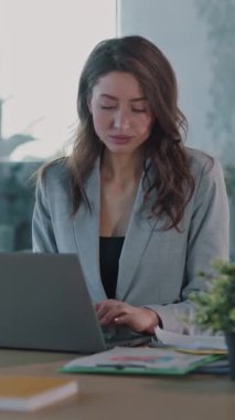 Kendini işine adamış bir iş kadını, modern ve parlak bir ofis ortamına dalmış, dikkatle dizüstü bilgisayarına odaklanır.