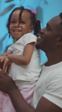 Bir adam şefkatli kollarında küçük bir kızı nazikçe tutuyor, sevgi ve mutlulukla dolu güzel bir an yaratıyor.