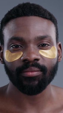 Genç bir adam lüks altın göz maskeleri takıyor. Çağdaş cilt bakımını ve kişisel bakım eğilimlerini etkili bir şekilde sergiliyor.