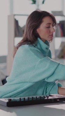 Odaklanmış bir ortamda, mavi kazaklı bir kadın masasında çalışıyor, dikkatle daktilo ediyor ve görevlerine daldırıyor, kendini adadığını gösteriyor.