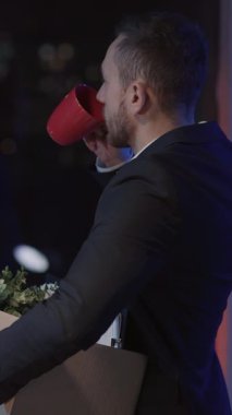 Neşeli genç beyaz adam Coronavirus yüzünden modern ofisten ayrılıyor. Pencere kenarındaki kahveyi yıkıyor ve düşünüyor. İş krizi konsepti.