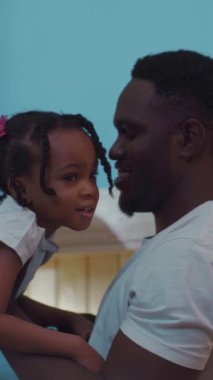 Bir adam küçük bir kızı kucaklarken dokunaklı bir sahne beliriyor. Şefkat ve bağlılık anı yakalıyor, aile sevgisini gösteriyor.