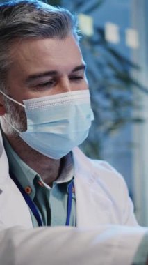 Gergin bir hastanede, bir doktor ağır sorumluluklarını vurgulayan kritik bir raporu gözden geçirir. Yakın plan, aciliyeti yansıtan maskeli bir adamı gösteriyor.