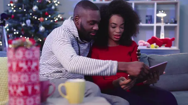 NEW YORK - 13 Aralık, 2017. Kırmızı kazaklı güzel kıvırcık kız kanepede oturuyor ve arka planda harika bir ağaç var. Tablet kullanan kız. Sarılmak..