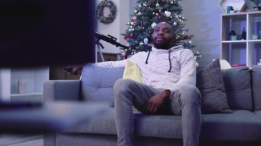 Televizyonda futbol maçı izleyen yakışıklı adam. Heyecanlı Afrikalı adam Noel ağacının arka planında favori takım oyununun tadını çıkarıyor. Kapalı.
