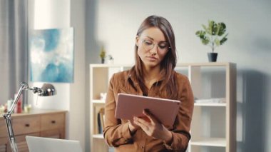 Tablet kullanarak son moda kahverengi gömlekli genç öğrenci ders çalışıyor. Gözlüklü güzel bir kız kameraya bakıyor ve gülümsüyor. Yakın plan..