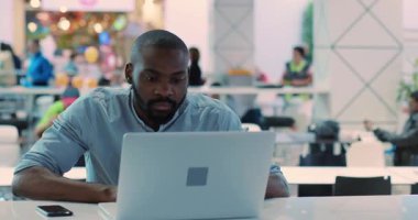 Yüzü kapatın, Afro-Amerikalı genç adam kafeteryada dizüstü bilgisayar kullanıyor. İnternetten alışveriş yapan internet adamı. Siyah iş adamı ağır çekimde oturuyor.