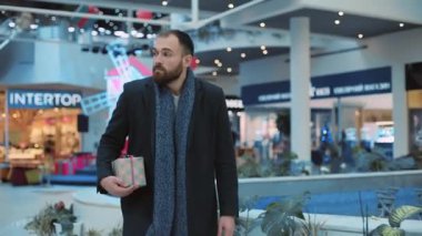 Elinde Noel hediyesi olan yakışıklı bir adam alışveriş merkezinin kutusundaki saate bakar ve acele eder. Yaklaş, al, dekore et. Akşam tatilleri hediyelik eşya dükkanları yavaş çekimde sürpriz yapar.