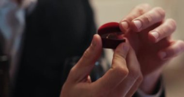 Sakallı, sakallı, kahverengi saçlı yakışıklı adam restoranda kırmızı elbiseli kıza evlenme teklif ediyor. Beyaz bir adam nişan yüzüğünü elinde tutuyor. Kur yapma.