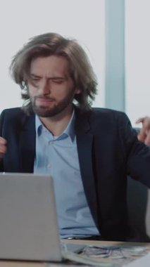 Takım elbiseli bir adam masasında dizüstü bilgisayarla çalışıyor. Saatini kontrol ederken verimlilik ve zaman yönetimini vurguluyor.
