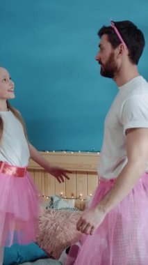Neşeli bir adam ve pembe etekli küçük bir kız kahkahalarla dolu bir dansı paylaşıyor, sevgi dolu bağlarını ve eğlencelerini sergiliyorlar.