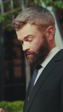 Başarılı bir iş adamı, şehir merkezinin kamerasında akıllı telefon standı kullanır. Sokak kameraları, mutlu yüz teknolojisi, cep telefonu giysisi, şehir modası, iş idarecisi, internet, açık hava günbatımı.