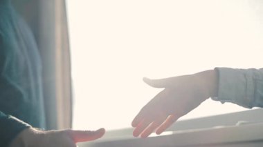 Pencerenin yanında el sıkışan iki beyaz genç insan. Genç çift kavgadan sonra barışıyor. Güneşli sabah.