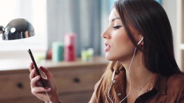 Güzel, genç Ukraynalı bir kadın masada oturmuş elinde akıllı bir telefonla kulaklıkla müzik dinliyor. Çekici kız şarkı söylüyor. Eğleniyorum. Yakın plan..