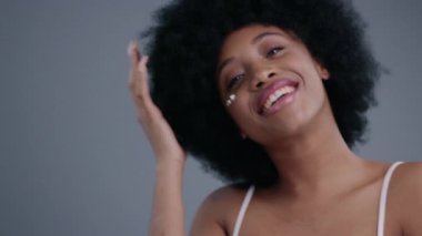 Afro saçlı neşeli genç kadın kameraya gülümsüyor gri arka planda izole edilmiş zamanının tadını çıkarıyor..