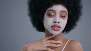 Yüzünde afro saç stili ve kozmetik maske olan harika bir güzellik modeli portresi. Siyahi Afrikalı kız göz kırpıyor ve gri arka planda kameraya gülümsüyor..