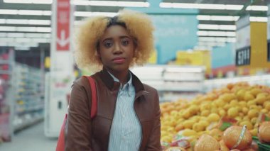 Mutlu Afro-Amerikan kadınları, süpermarket alışverişinde meyvenin yanındaki kameraya bakıp gülümserler. Siyahi çalışan tüketici ailesi yeni market portresi alır. Karışık müşteriler yavaş çekimde yaklaşır.