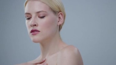 Çıplak omuzlu, elleri göğsünde kameraya bakan harika bir spa mankeni sarışın kız. Gri arka planda izole edilmiş, şehvetli, çıplak, çekici genç bir kadının portresi..