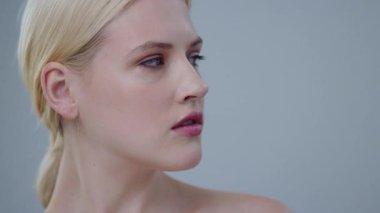 Stüdyoda poz veren çarpıcı sarışın kadının çıplak portresi. Güzel bir kızın, sağlıklı, parlak cildine dokunduğu ve kamerada gülümsediği yakın plan..