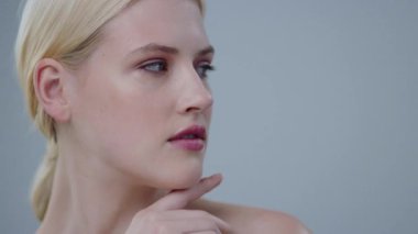 Gri arka planda gülümseyen parlak melek yüzlü çarpıcı sarışın kız. Kamera önünde poz veren saf ve şehvetli kadın portresi..