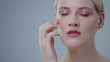 Muhteşem sarışın kadın narin tenine dokunuyor narin elleriyle ve geniş bir gülümsemeyle. Gri arka planda güzellik kaplıcası portresi.